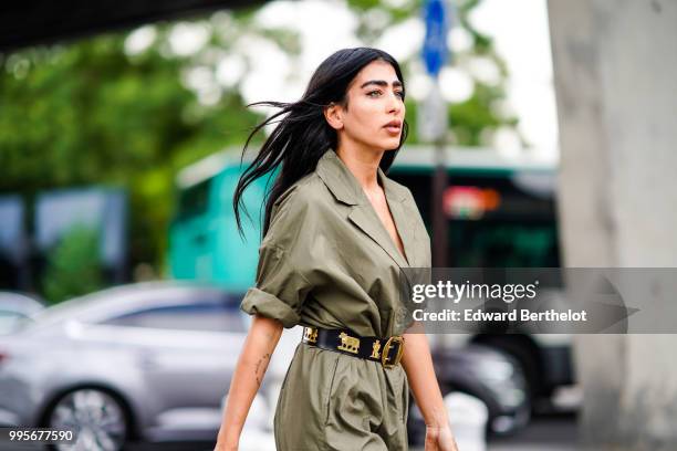 Guest wears a green khaki trench coat dress, a black leather belt with golden part, white sneakers shoes , outside Vetements, during Paris Fashion...