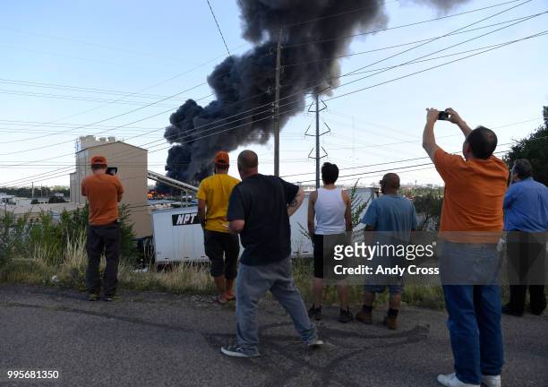 Onlookers get on angle on a fire in a large pile of crushed vehicles near 5600 York St. July 10, 2018.