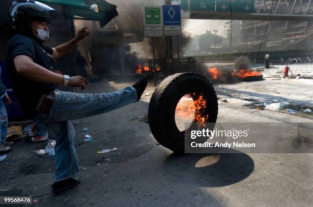 Anti-government red shirt protester adds to a burning pile of tires during street clashes as the violence in central part of the city escalates on...