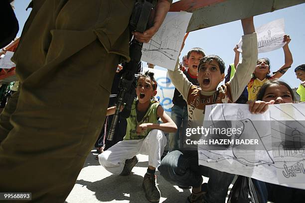 Palestinian children hold up their drawings and shout slogans at an Israeli checkpoint during a peaceful demonstration on May 15, 2010 in the...