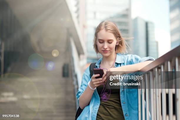 una giovane donna attraente di 20 anni con un telefono cellulare e cuffie che ascoltano la musica - 20 24 years photos foto e immagini stock