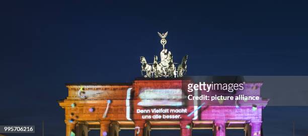Spectators look on at the illuminated Brandenburg Gate with the writing 'Denn Vielfalt macht uns alle besser' projected against the facade during the...