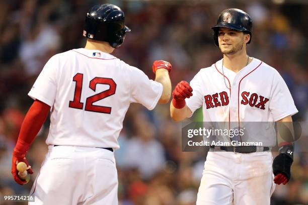 Andrew Benintendi of the Boston Red Sox high fives Brock Holt as he returns to the dugout after scoring in the third inning a game against the Texas...