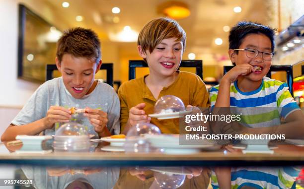 3 boys of diverse ethnicities enjoying all you can eat asian food in running sushi restaurant - ems photos et images de collection