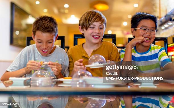 3 boys of diverse ethnicities enjoying all you can eat asian food in running sushi restaurant - ems forster productions 個照片及圖片檔