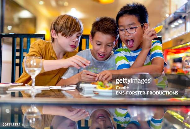 3 boys of diverse ethnicities enjoying themselves in running sushi restaurant - ems stockfoto's en -beelden
