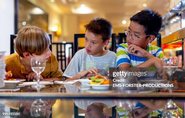 3 boys of diverse ethnicities enjoying all you can eat asian food in running sushi restaurant - ems forster productions stock pictures, royalty-free photos & images