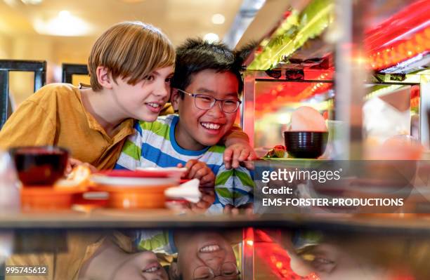 two 10 years old boys in sushi restaurant - sushi train stock pictures, royalty-free photos & images