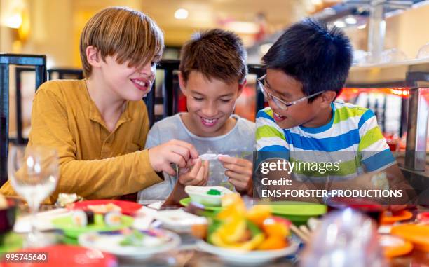 3 boys of diverse ethnicities enjoying all you can eat asian food in running sushi restaurant - ems stockfoto's en -beelden