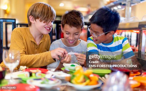 3 boys of diverse ethnicities enjoying all you can eat asian food in running sushi restaurant - ems forster productions stock pictures, royalty-free photos & images