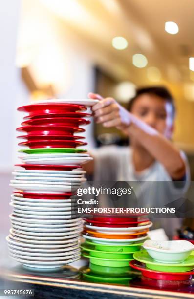 boy stacking plastic plates towering in sushi bar - ems stockfoto's en -beelden