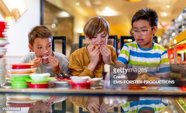 3 boys of diverse ethnicities enjoying all you can eat asian food in running sushi restaurant - ems forster productions 個照片及圖片檔