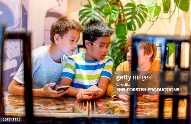 3 boys of diverse ethnicities with smart phones in restaurant - ems stockfoto's en -beelden