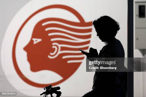 Cyclist is silhouetted as she uses her smartphone in front of an Idemitsu Kosan Co. Gasoline station in Tokyo, Japan, on Tuesday, July 10, 2018....