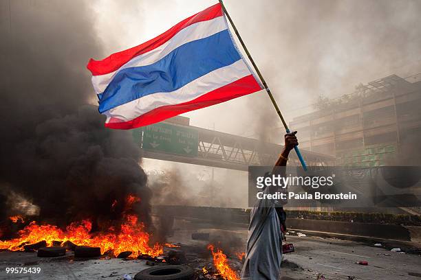 Red shirt protester carries the Thai flag as tires burn and the violence in central part of the city escalates on May 15, 2010 in Bangkok, Thailand....