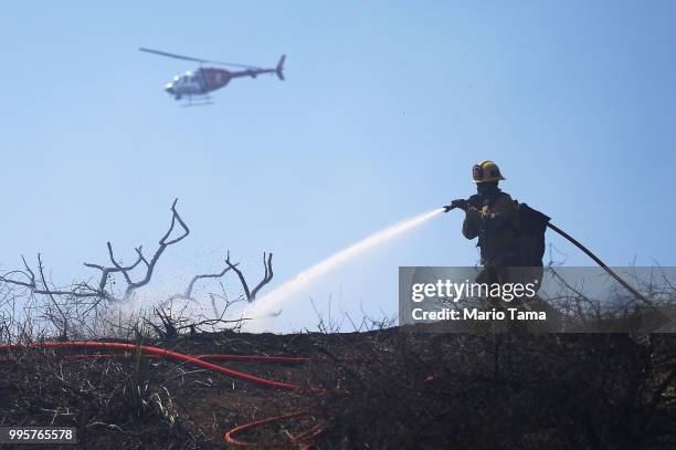 Firefighter works on the Griffith fire at Griffith Park, with a helicopter working in the background, on July 10, 2018 in Los Angeles, California....