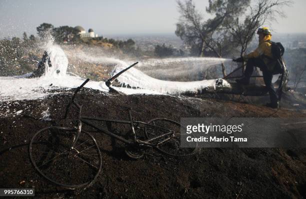 Firefighter works on the Griffith fire at Griffith Park, with a charred bicycle in the foregound, on July 10, 2018 in Los Angeles, California....