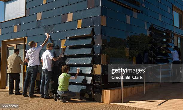 Members of Team Germany wipe down the solar cell panels which serve as the external wall of their two-story solar house in preparation for the...