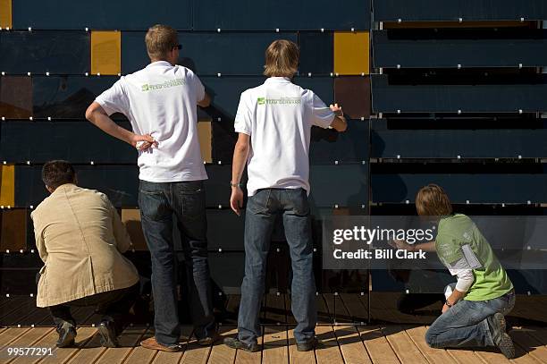 Members of Team Germany wipe down the solar cell panels which serve as the external wall of their two-story solar house in preparation for the...