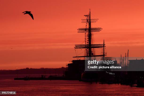 The sky appears red during sunrise above the 4 mast passat ship in Travemuende, Germany, 03 October 2017. Photo: Maurizio Gambarini/dpa