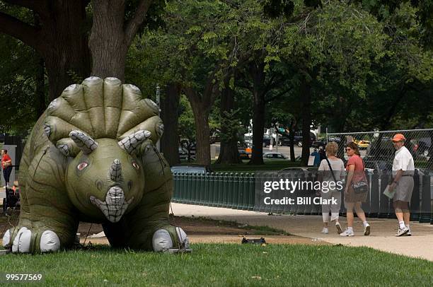 Tourists stare at an inflatable stegosaurus as they walk down the sidewalk lining Consitution Ave. NW along Upper Senate Park on Wednesday, June 20,...