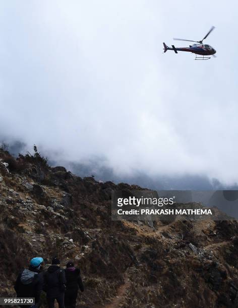 In this photograph taken on April 17 hikers walk on a trail as a helicopter comes in to land at Mong La village near Namche Bazar on the route to...