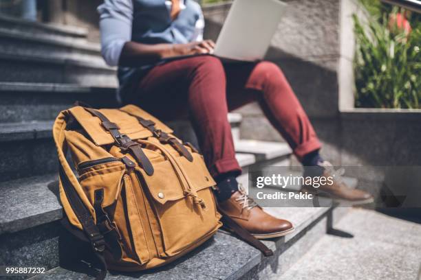 man surfing the net on his laptop - backpack stock pictures, royalty-free photos & images