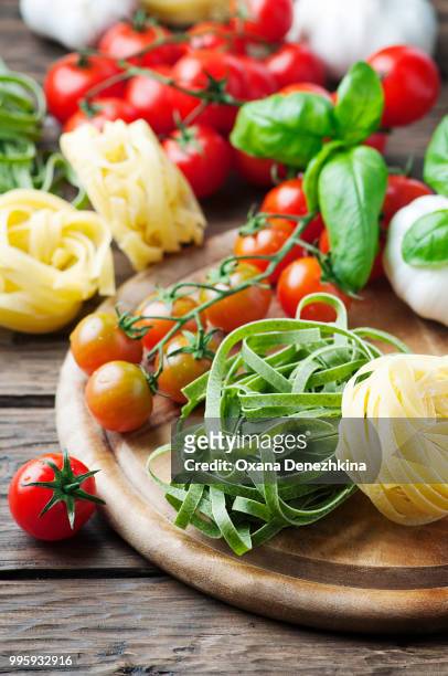 raw pasta, tomato and basil on the wooden table - tomato pasta stock pictures, royalty-free photos & images