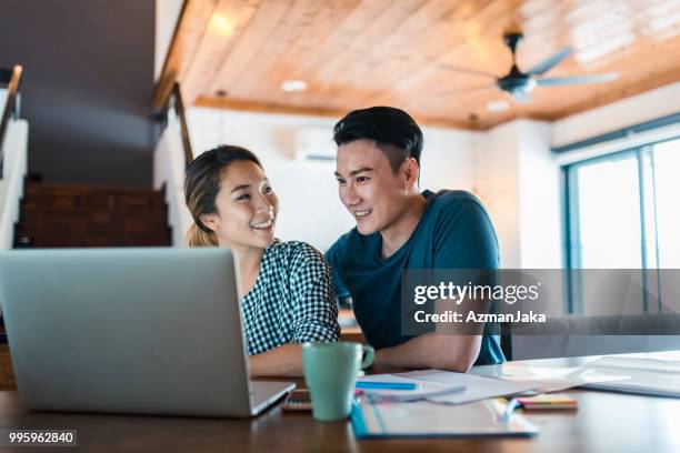 chinese couple using a laptop in the living room and planning a vacation - asian man home laptop stock pictures, royalty-free photos & images