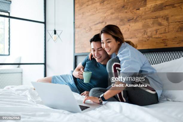 chinese couple drinking coffee and using laptop in bed - asian young couple stock pictures, royalty-free photos & images