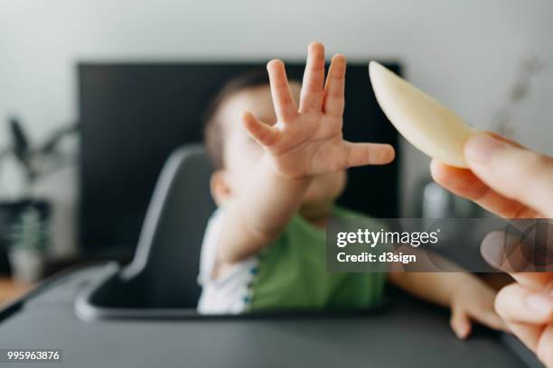 hungry baby sitting on highchair reaching for a slice of fruit from mother's hand - baby eating vegetables stock pictures, royalty-free photos & images