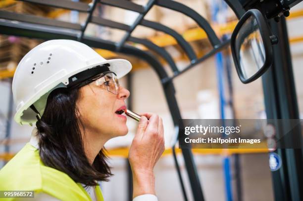 senior warehouse woman worker looking in the mirror, applying lipstick. - halfpoint stockfoto's en -beelden