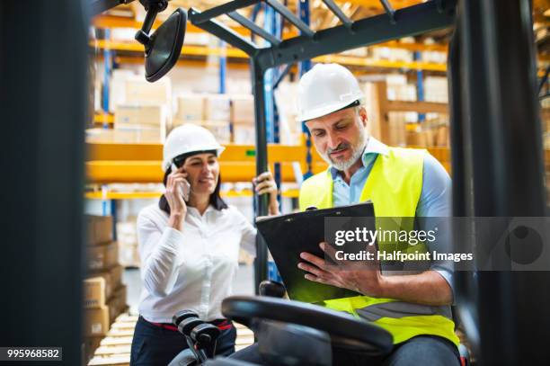 mature male worker with clipboard making notes and a senior manager with smart phone, making a phone call. - halfpoint stockfoto's en -beelden
