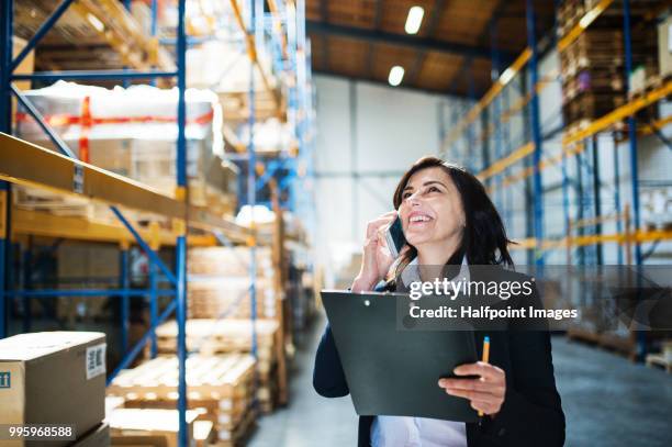 senior warehouse woman manager or supervisor with smart phone making a phone call. - halfpoint stockfoto's en -beelden