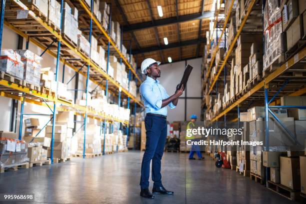 mature man manager in blue shirt with clipboard in a warehouse. - halfpoint stock-fotos und bilder