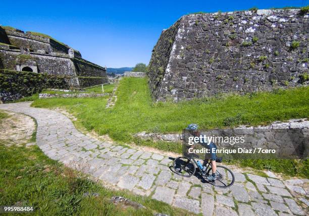 cyclist riding in between the walls of valença do minho fortress - white spandex shorts stockfoto's en -beelden