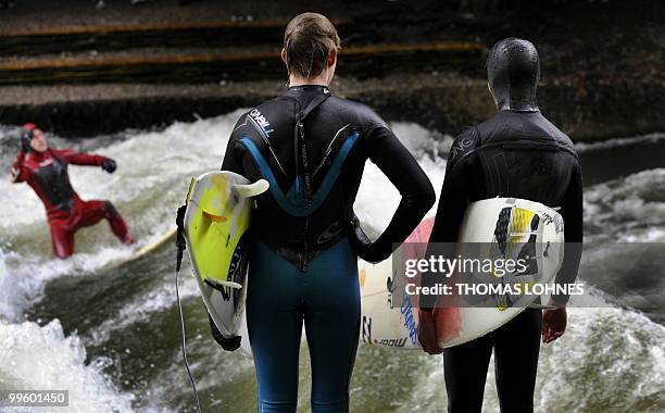 Two surfers watch as a man surfs on a wave made by the fast moving water of the River Isar in the southern German city of Munich on May 15, 2010....