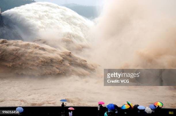 People watch as water and sand is blasted from the Xiaolangdi Dam on the Yellow River on July 4, 2018 in Jiyuan, Henan Province of China. A round of...