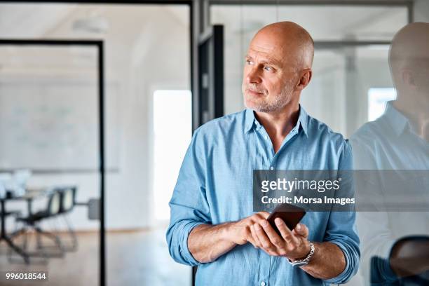 thoughtful manager with smart phone at office - completely bald stock photos et images de collection