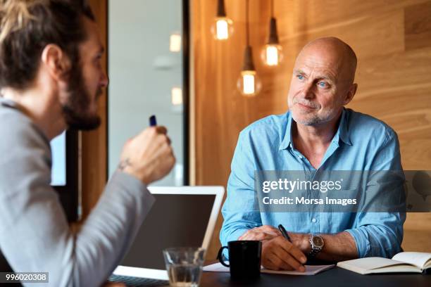 businessman listening to colleague at table - mid volwassen mannen stockfoto's en -beelden