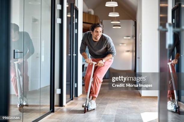 businessman enjoying on push scooter in office - cómico fotografías e imágenes de stock