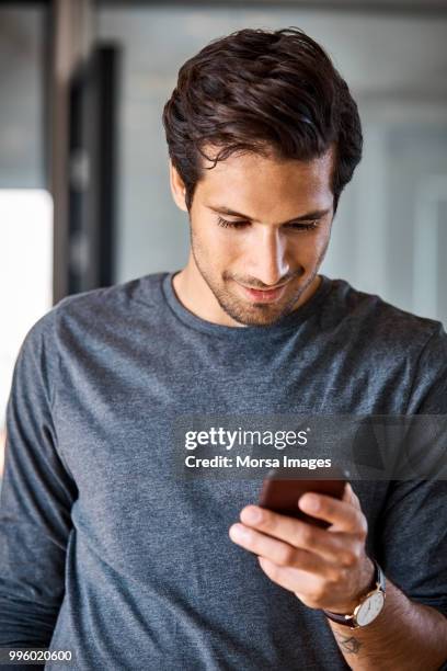 smiling businessman using mobile phone at office - business man looking at smart phone stock-fotos und bilder