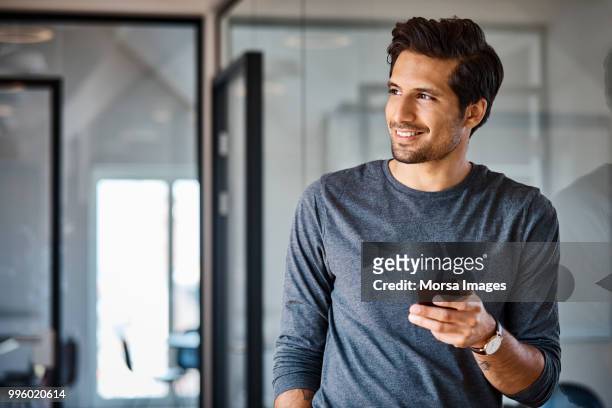 smiling businessman with mobile phone looking away - business man looking at smart phone stock-fotos und bilder