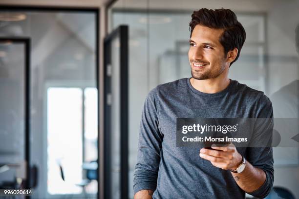 smiling businessman with mobile phone looking away - man holding phone imagens e fotografias de stock