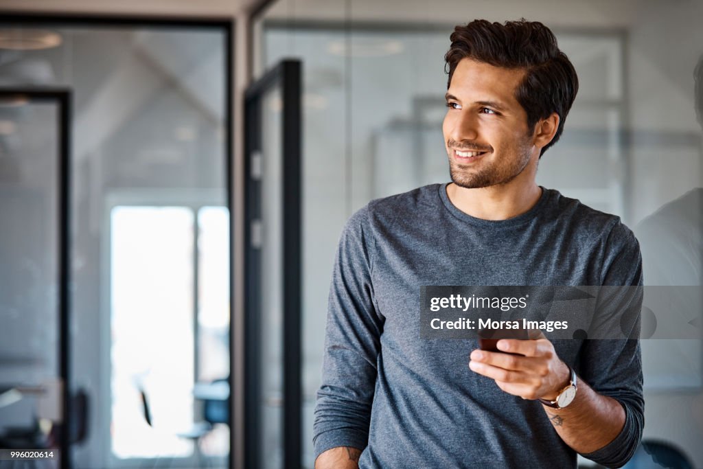 Smiling businessman with mobile phone looking away