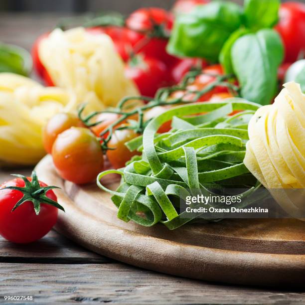 raw pasta, tomato and basil on the wooden table - tomato pasta stock pictures, royalty-free photos & images