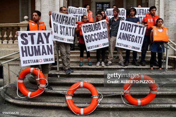 "We remain human" network activists hold banners as they are chained on the steps of the Ministry of Transport to protest against the Italian...