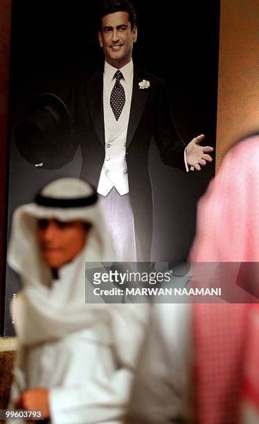Saudis walks past a picture of Lebanese politician Mosbah Ahdab posing in a suit created by Lebanese designer Michael Fenici at a fashion show in...