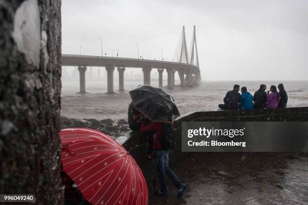 People use umbrellas to shield themselves from the rain as the Bandra-World Sea Link bridge stands in the background in the suburb of Bandra in...