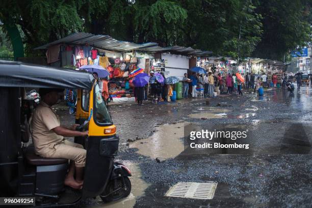 An auto-rickshaw drives through flooded potholes past a market in the suburb of Bandra in Mumbai, India, on Tuesday, July 10, 2018. The monsoon is...